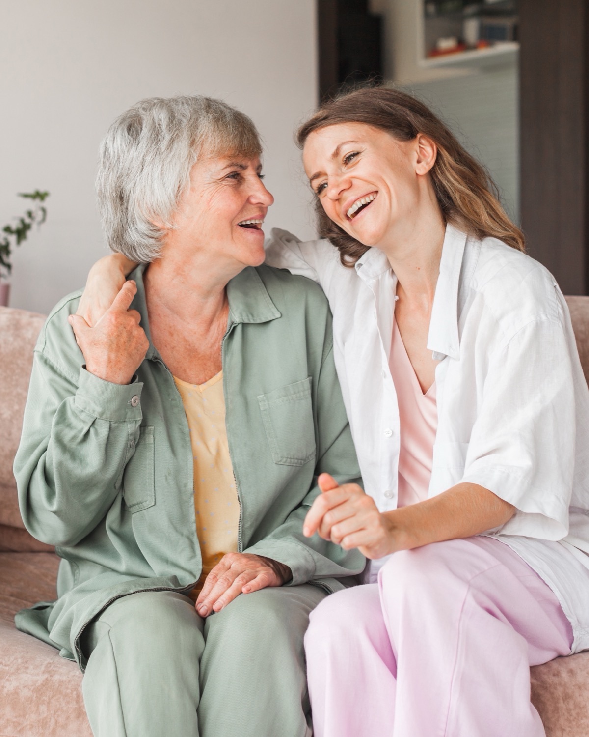 An adult daughter and her mother laughing together on a couch